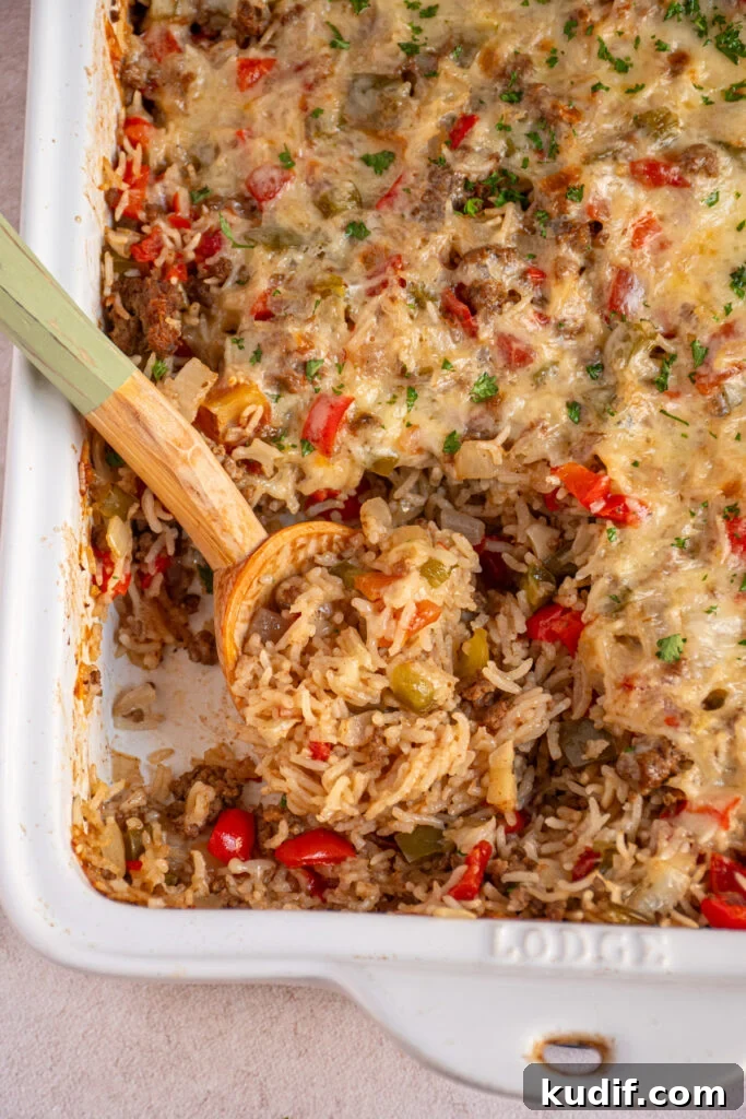 Cheesy Stuffed Pepper Casserole Bake Recipe 3 A white dish filled with stuffed pepper casserole with a wooden spoon showing rice, beef, and peppers.
