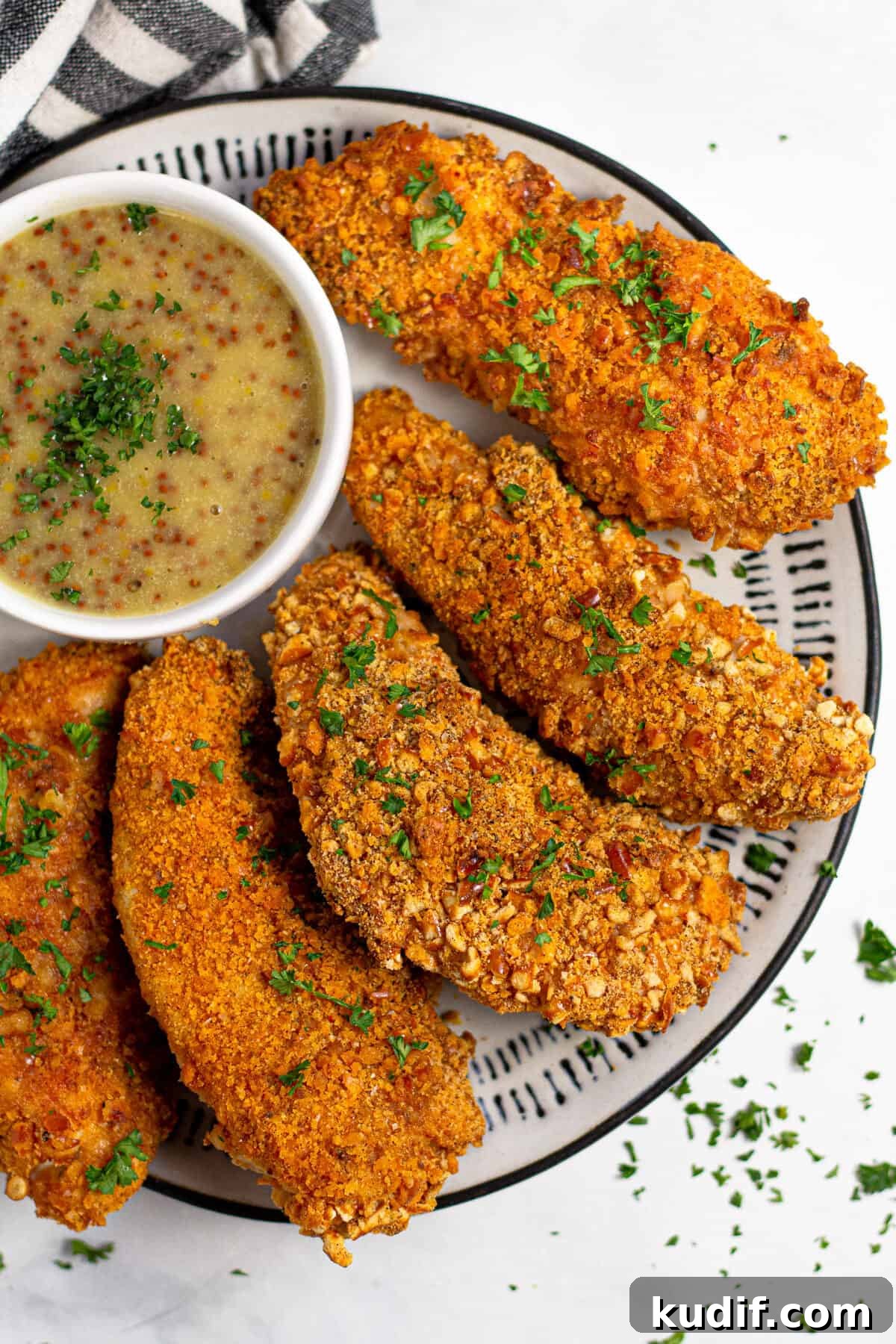 Overhead shot of baked chicken tenders on a white plate garnished with fresh parsley 