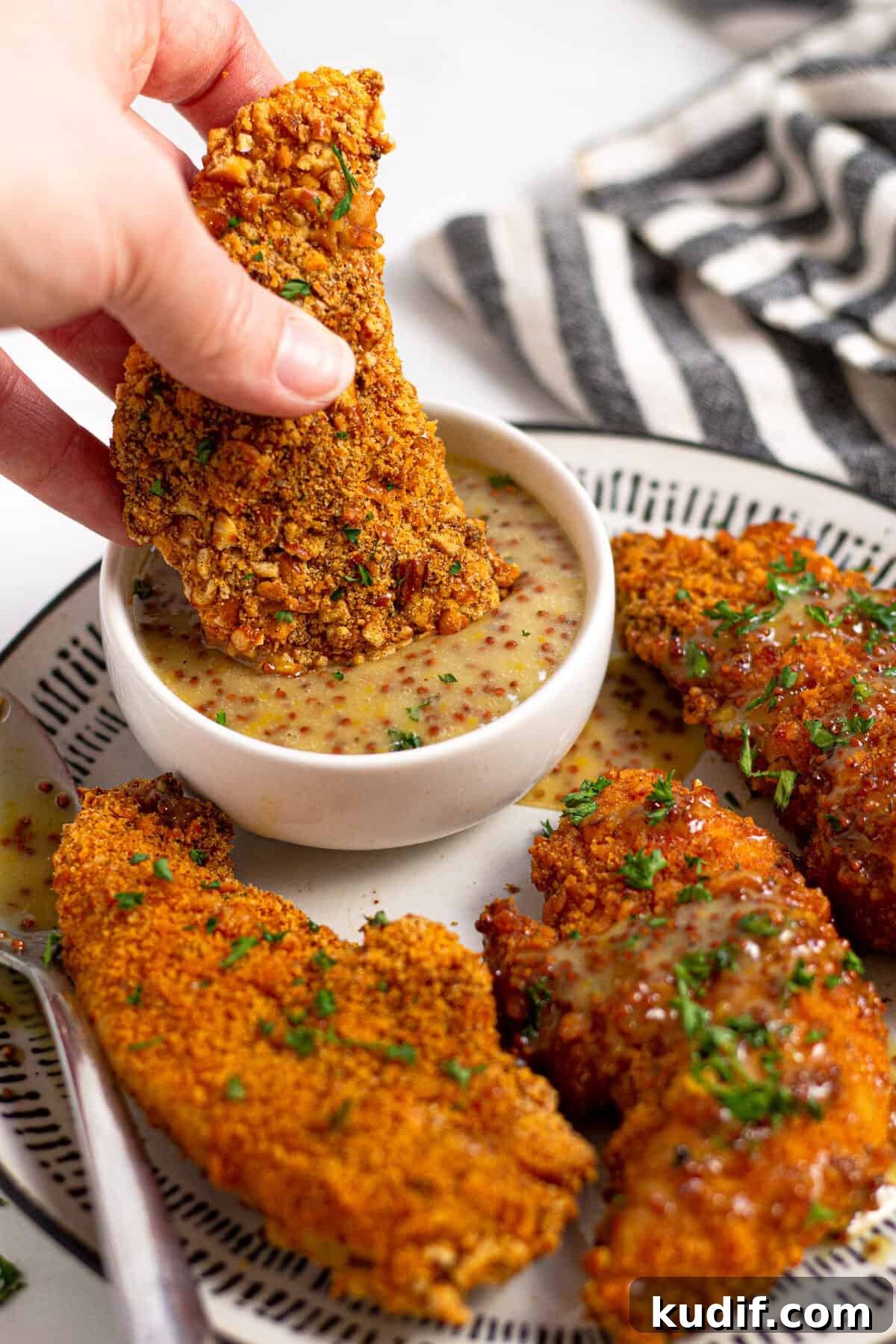 Close up shot of a baked chicken tender being dunked into honey mustard sauce 