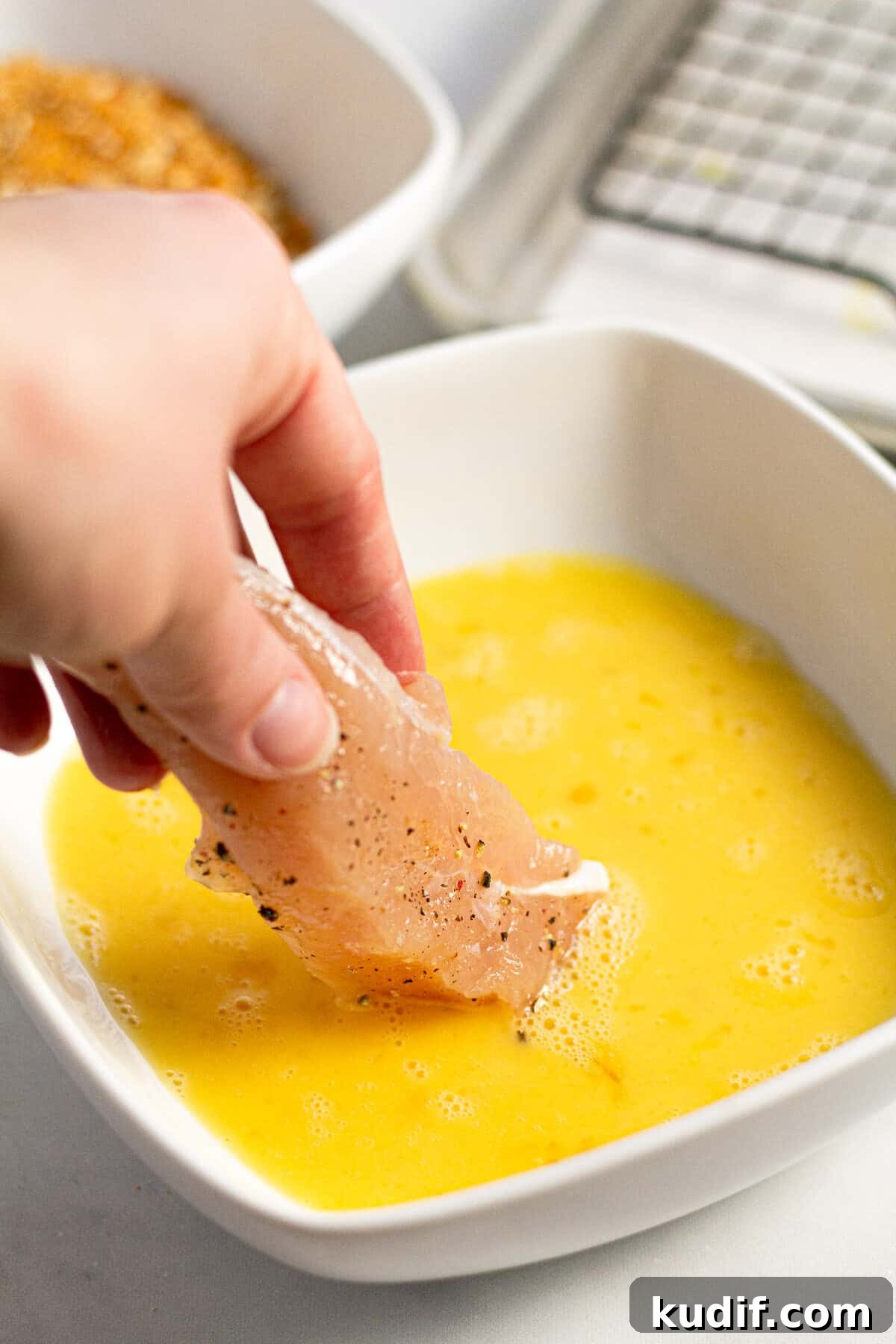 A chicken tender being dipped in an egg wash 