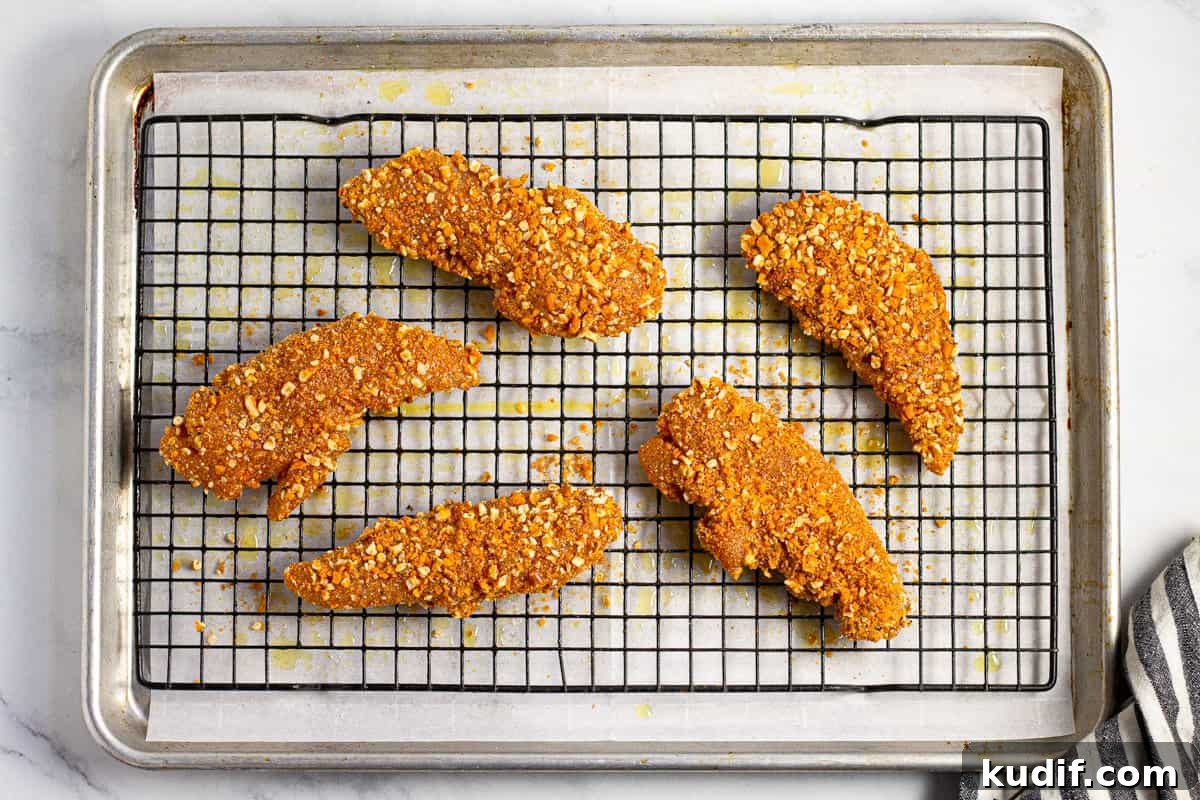 Breaded chicken tenders on a cooling rack on a parchment lined baking sheet