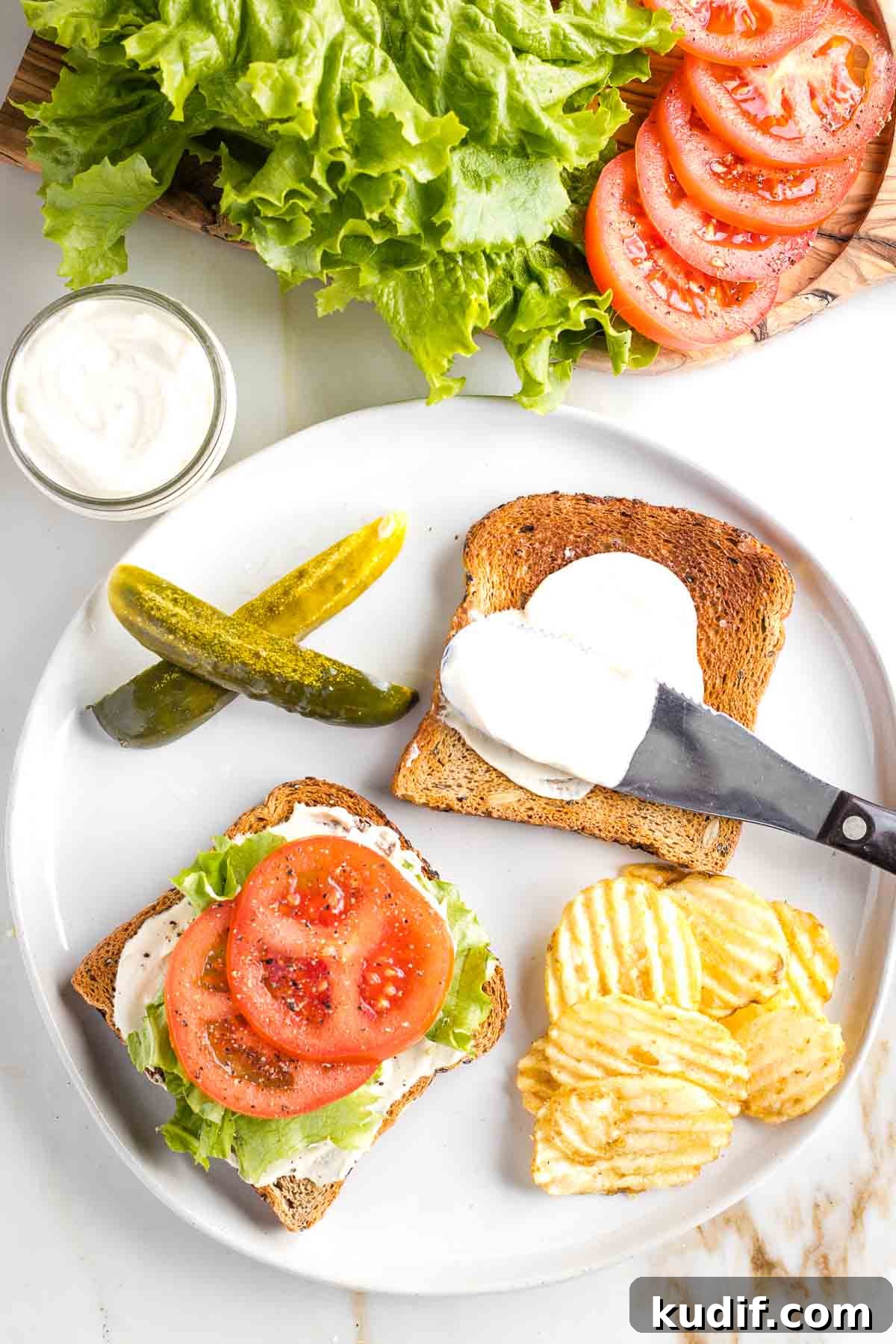 Creamy Tofu Vegan Mayonnaise Recipe — Quick & Luscious 2 Toasted bread with mayonnaise, lettuce and tomato, with a side of pickles and chips.