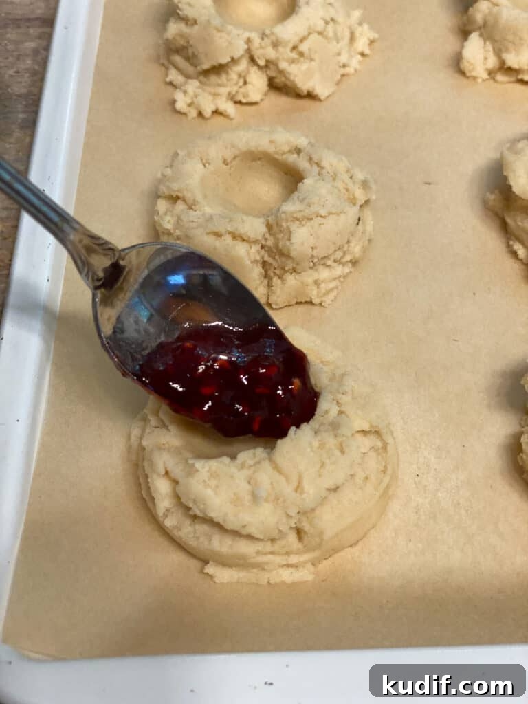 Raspberry Jam Thumbprint Cookies Recipe for Soft, Buttery Cookies 15 process shot of adding raspberry jam to dent in dough