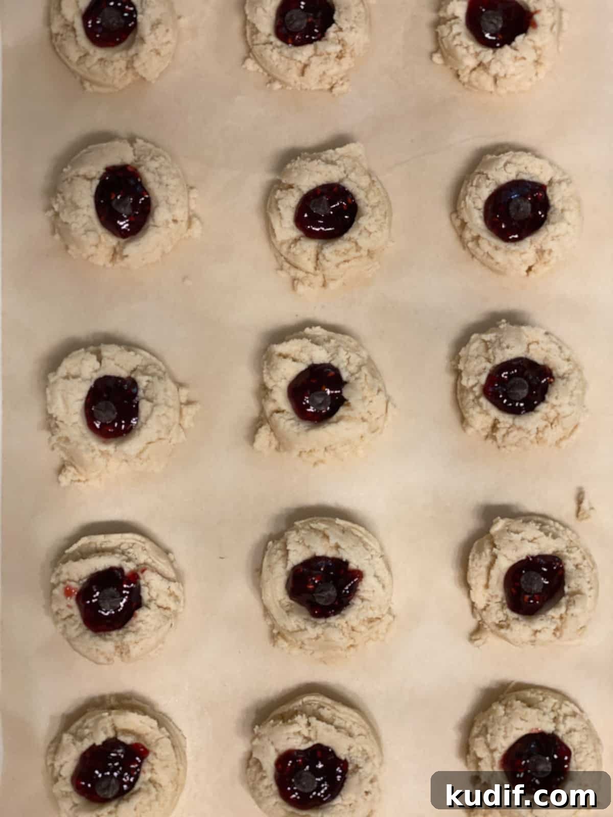 Raspberry Jam Thumbprint Cookies Recipe for Soft, Buttery Cookies 17 pre baked Raspberry Jam Thumbprint Cookies scattered on a baking sheet