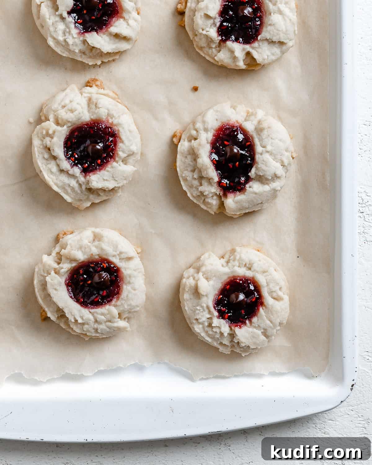 Raspberry Jam Thumbprint Cookies Recipe for Soft, Buttery Cookies 18 completed Raspberry Jam Thumbprint Cookies scattered on a baking sheet