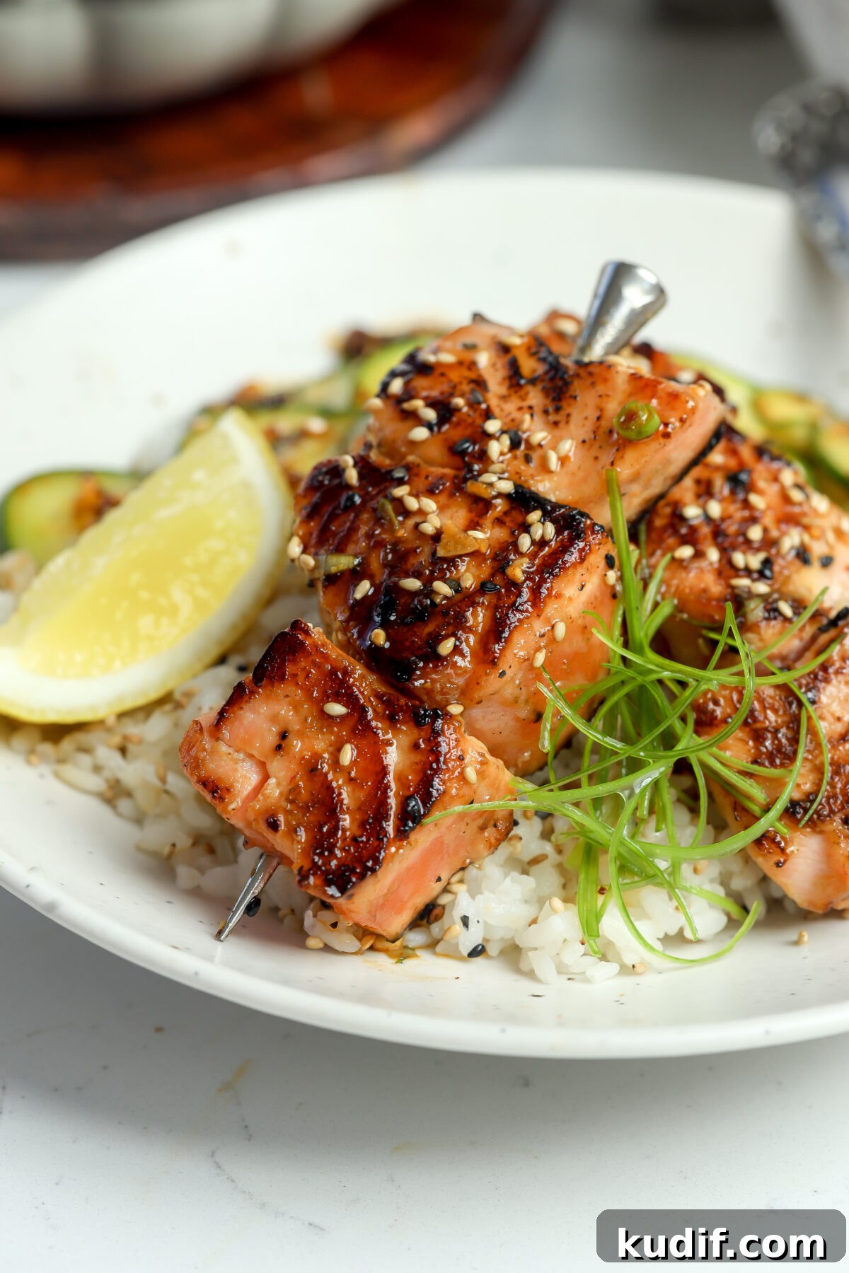 Miso-Glazed Salmon Skewers with Sesame and Scallions 8 A recipe for Miso glazed salmon skewers on a bed of rice next to sliced lemon.