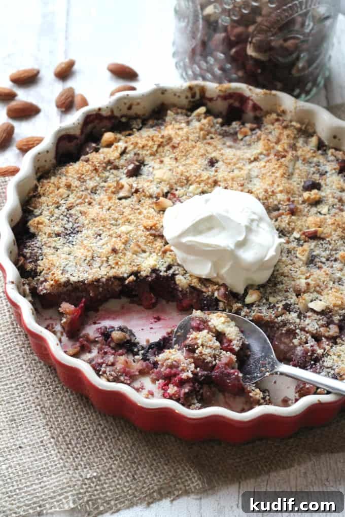 no grain berry apple crumble in a red ovenproof dish with a dollop of cream on top