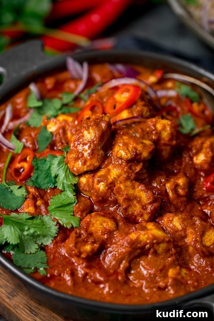 Authentic Chicken Madras Curry Recipe for Bold Flavor 7 Close up of chicken madras in a dark bowl. The madras is topped with sliced coriander, red onion and red chillies.