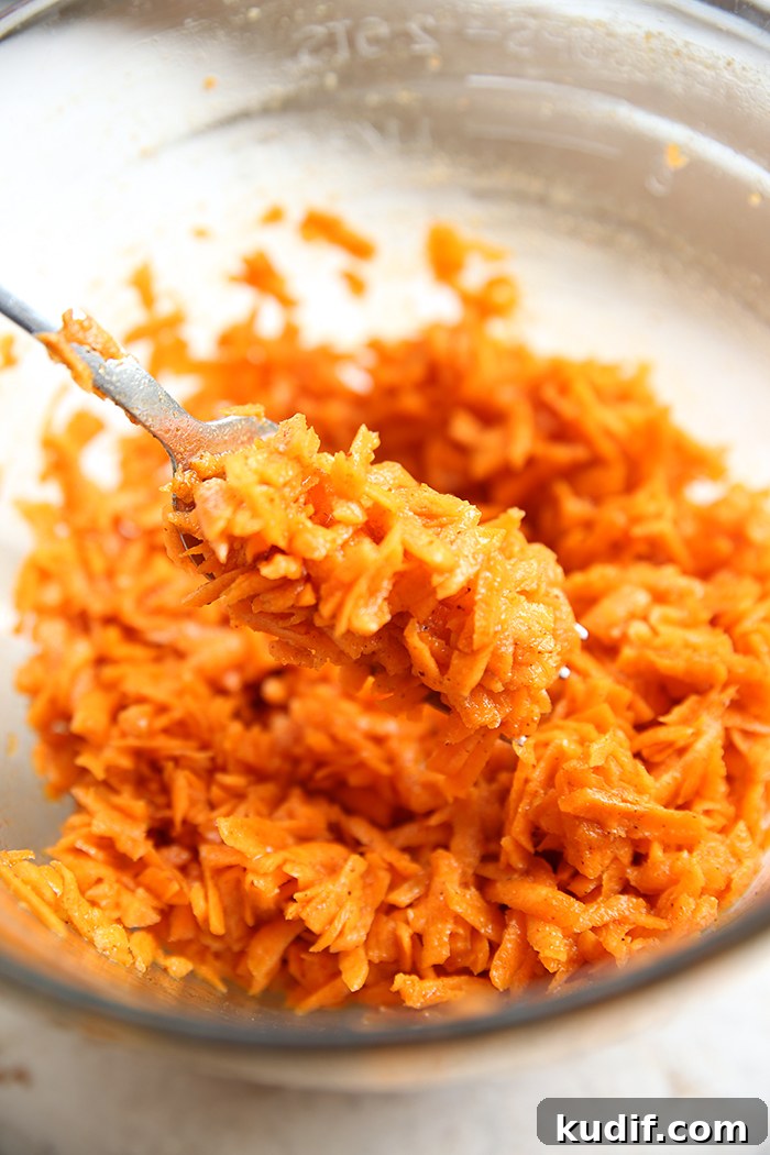 Carrot Kimchi in a glass mixing bowl with a spoon held above from the left with a scoop of carrot kimchi.