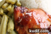A white plate with a serving of green beans, white rice, and a sweet and sour chicken thigh.