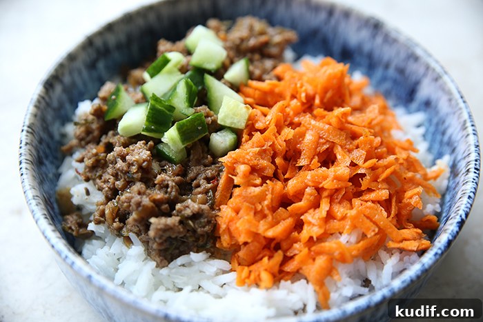 A bowl with white rice with ground beef, diced cucumber, and carrot kimchi.