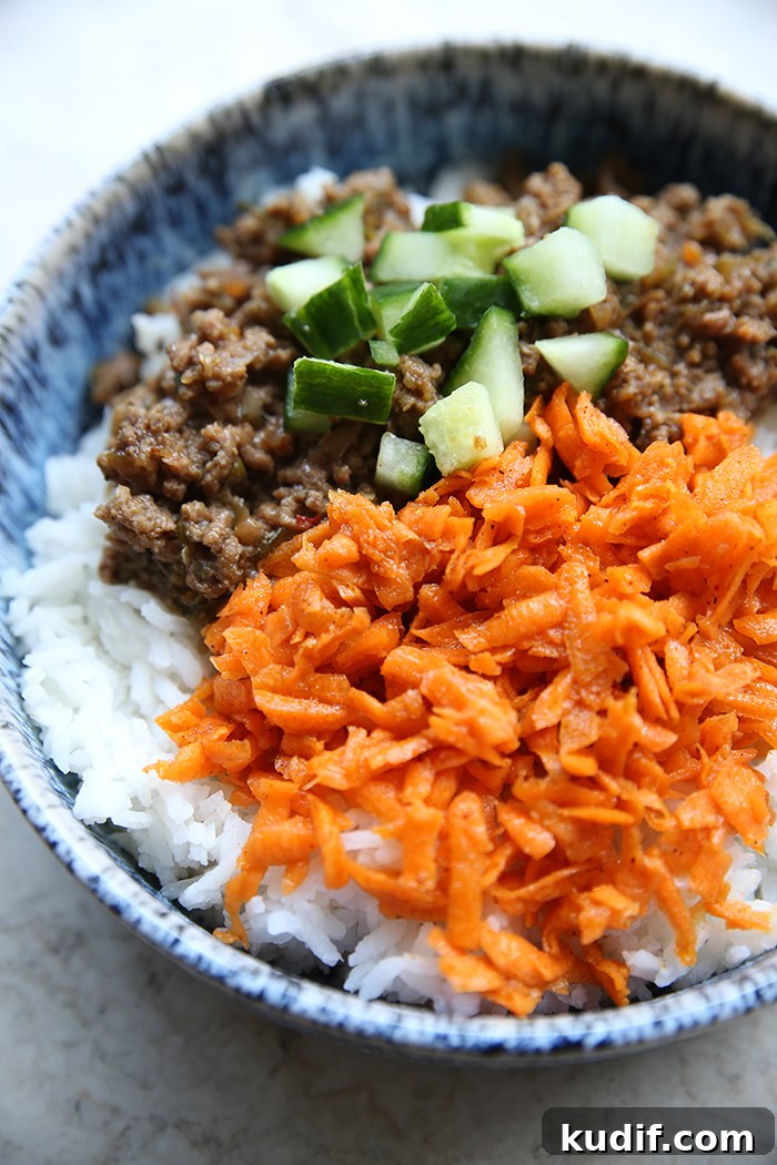 A bowl of white rice with carrot kimchi, ground beef, and chopped cucumber.