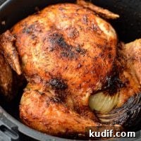 A whole chicken, cooked in an air fryer basket with crispy skin.