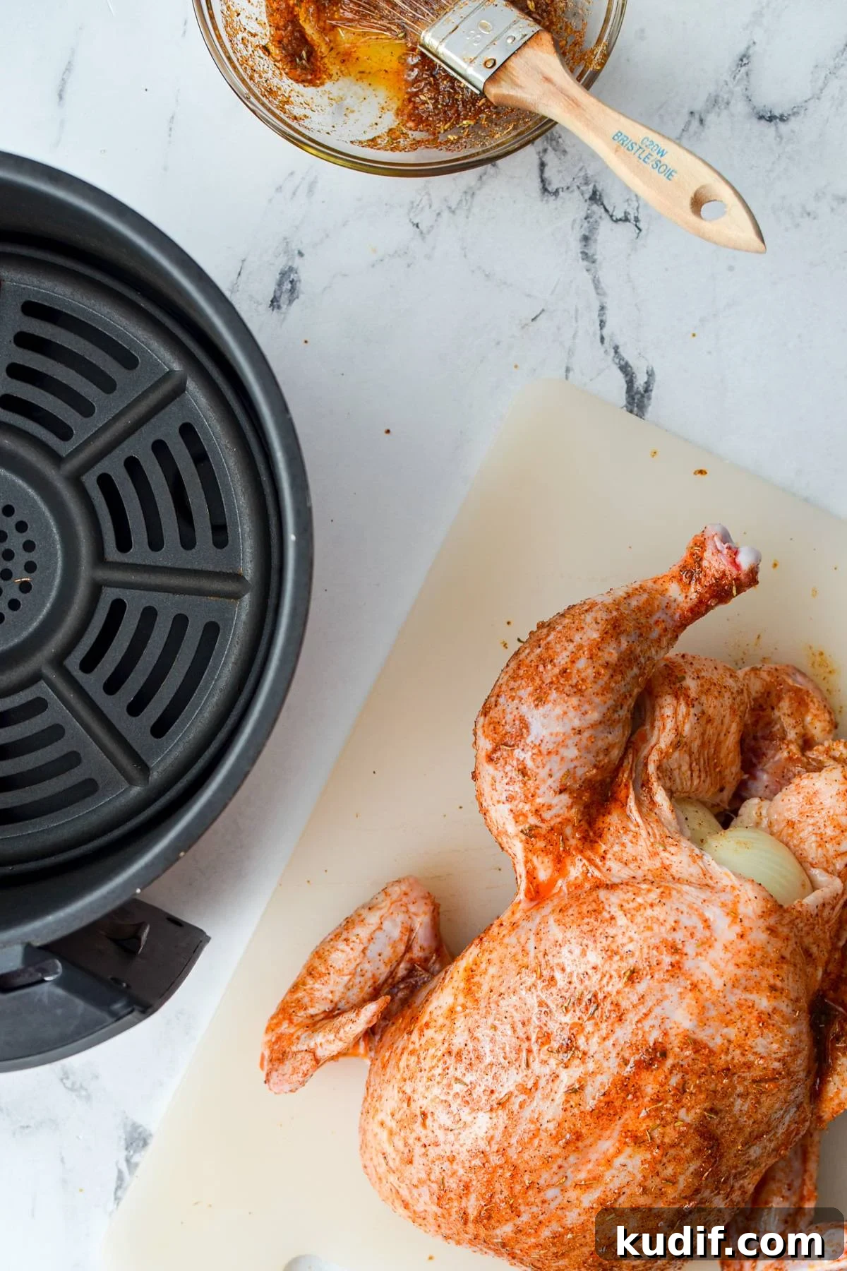 Rotisserie-Style Whole Chicken in the Air Fryer 8 A whole chicken brushed with a spice rub, with an air fryer basket on the side.