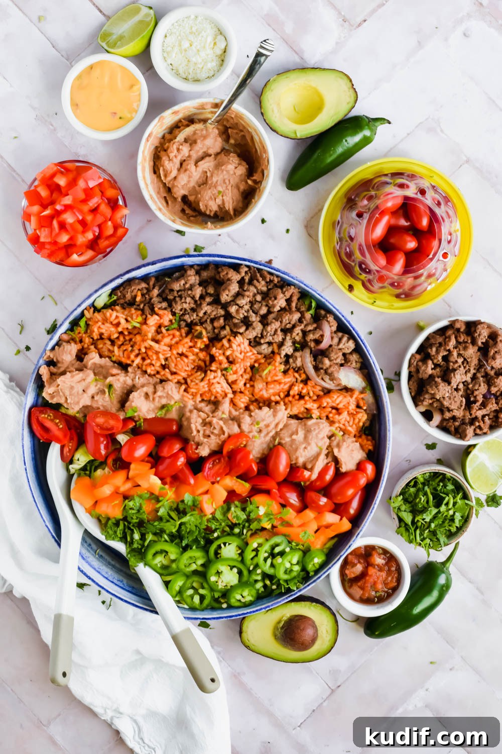 Healthy 7 layer salad in a large bowl with ground beef, rice, beans, tomatoes, peppers, cilantro, and jalapeño on top.