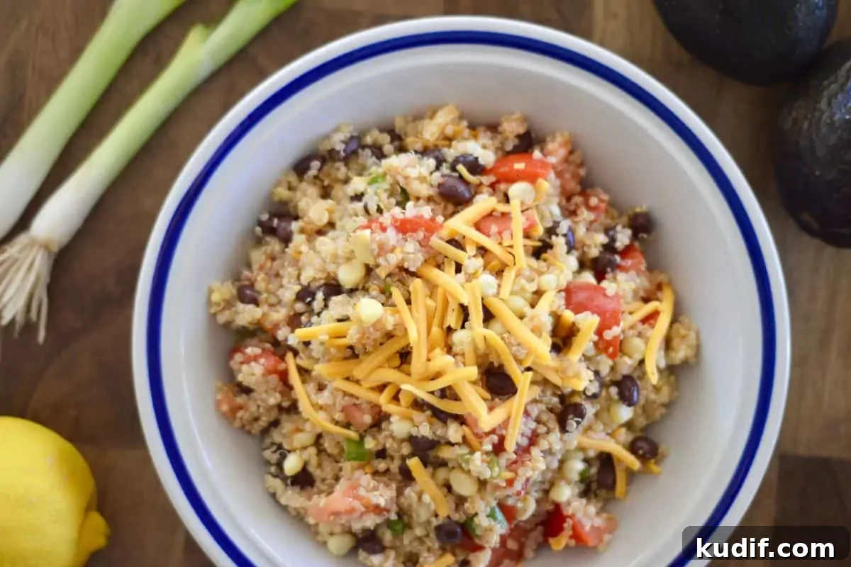 Mexican-Style Quinoa Salad with Corn, Black Beans & Lime Dressing 6 Recipe in a white bowl with green onions and lemon next to it.