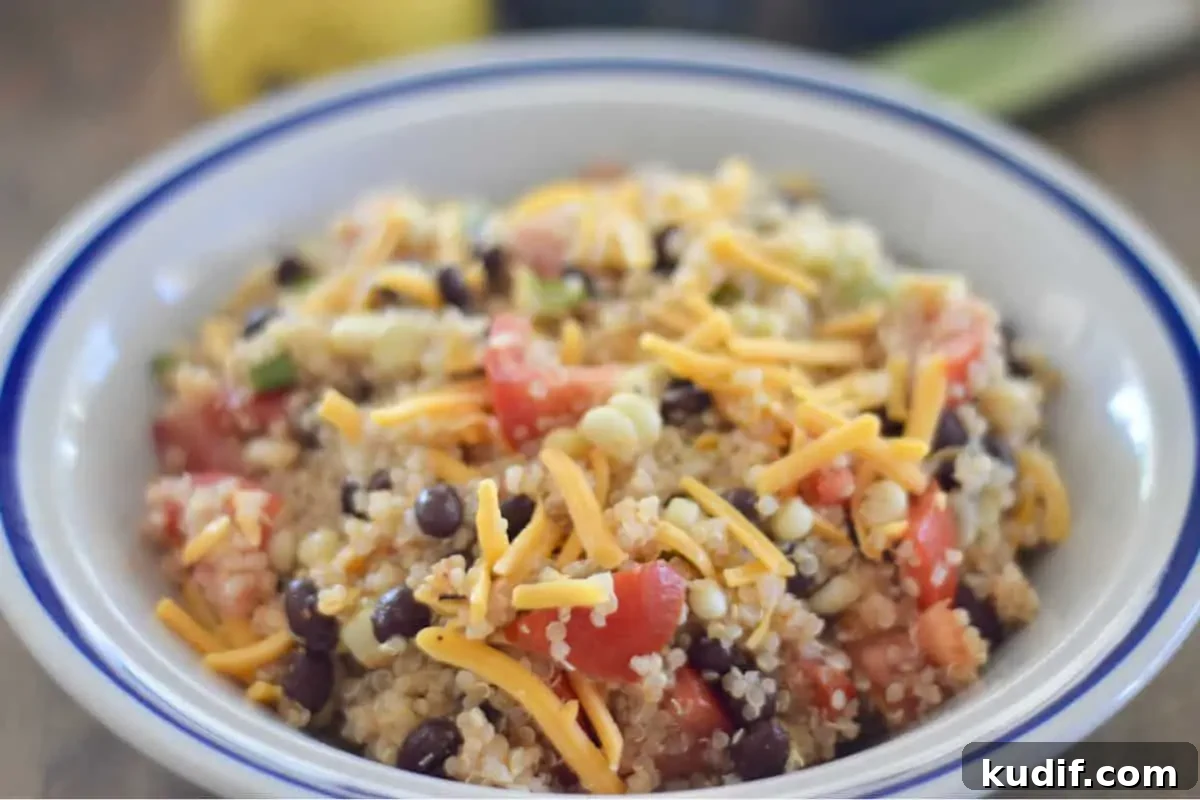 Mexican-Style Quinoa Salad with Corn, Black Beans & Lime Dressing 3 White bowl with a blue trim holding the recipe topped with shredded cheddar cheese.