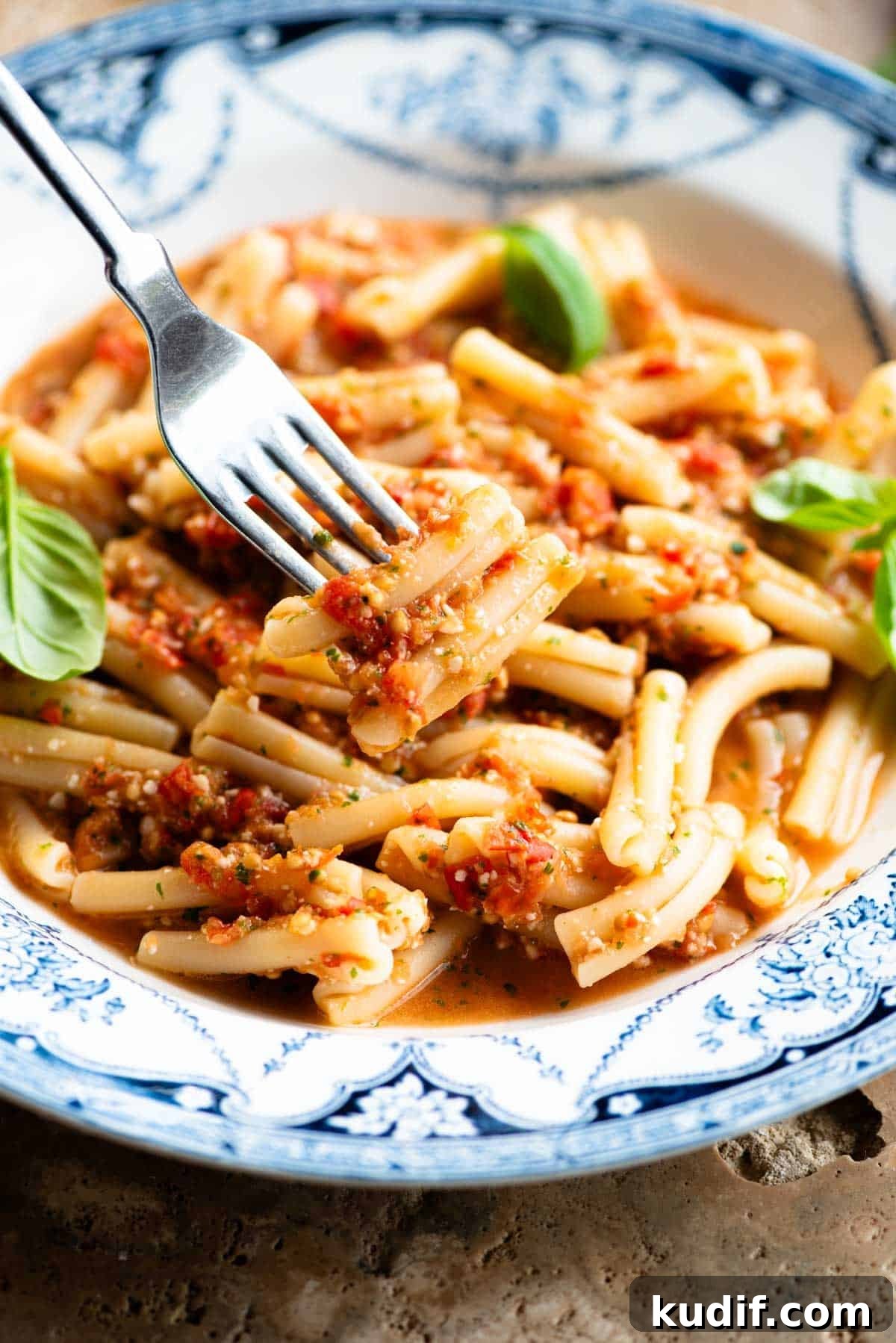 Fresh No-Cook Tomato Pasta Sauce Recipe for Quick Dinners 5 A close up of a fork holing some pasta with a fresh tomato sauce in a blue and white bowl.