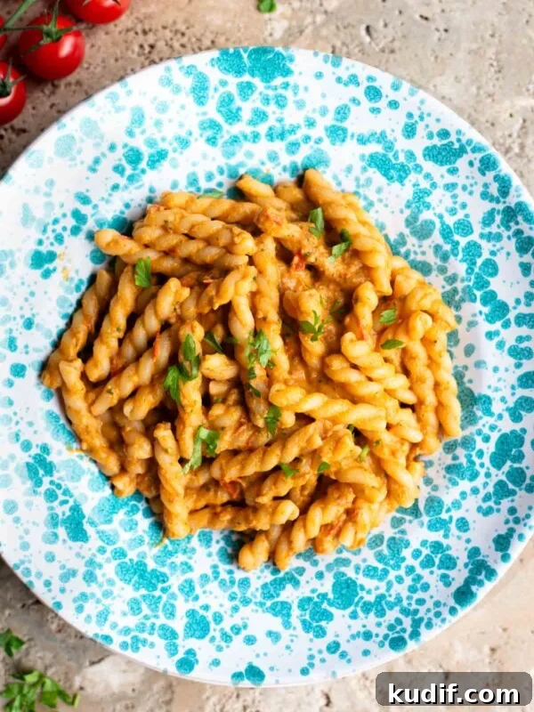 Fresh No-Cook Tomato Pasta Sauce Recipe for Quick Dinners 6 Pasta in a tuna tomato sauce in a blue and white spotted plate sitting on a travertine surface.