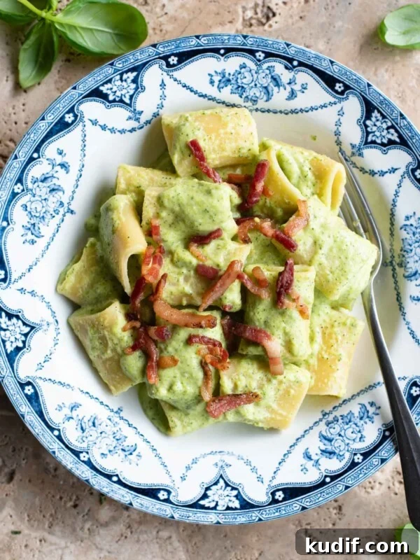 Fresh No-Cook Tomato Pasta Sauce Recipe for Quick Dinners 7 A creamy zucchini pasta in a blue and white bowl topped with crispy pancetta sitting on a travertine surface.