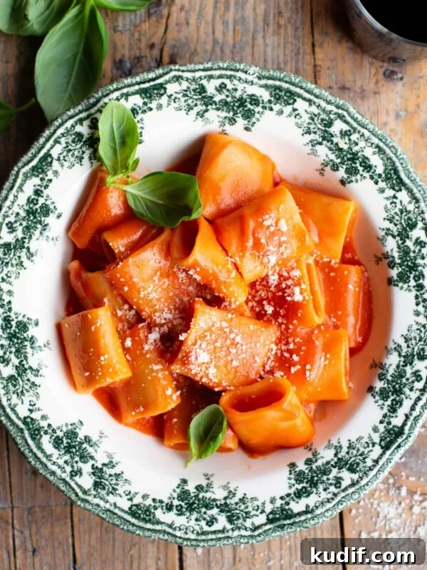 Fresh No-Cook Tomato Pasta Sauce Recipe for Quick Dinners 8 Paccheri pasta with a smooth tomato sauce in a green and white patterned bowl topped with basil.