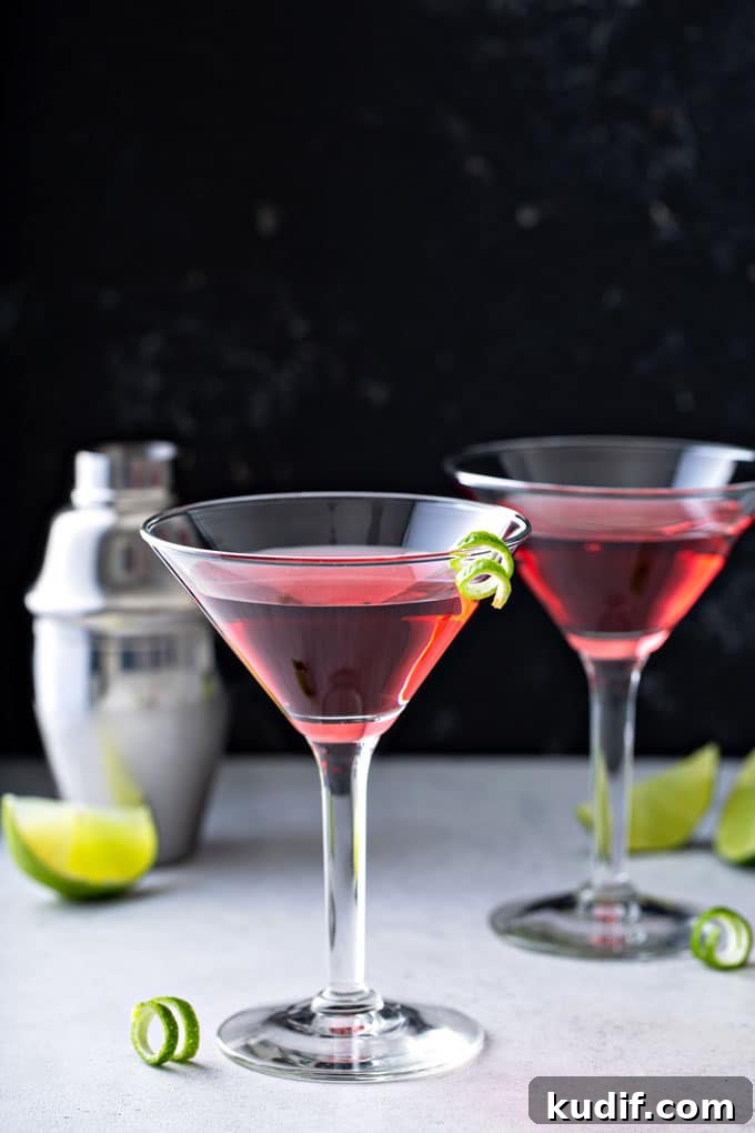 Classic Cosmopolitan Cocktail Recipe: How to Mix the Perfect Cosmo 4 A couple of cosmopolitan cocktails on a white surface next to a cocktail shaker