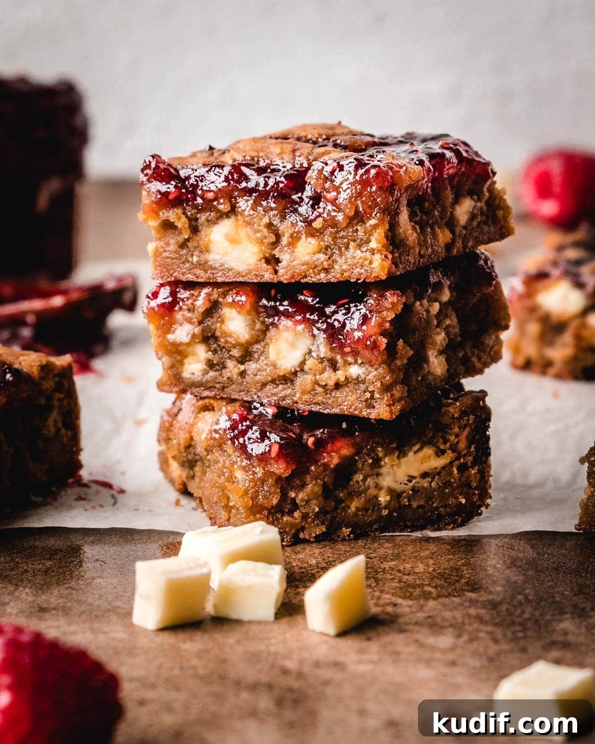 White Chocolate Raspberry Blondies with Tangy Fruit Swirls 2 Stack of white chocolate and raspberry blondie squares with white chocolate chunks laying around them.