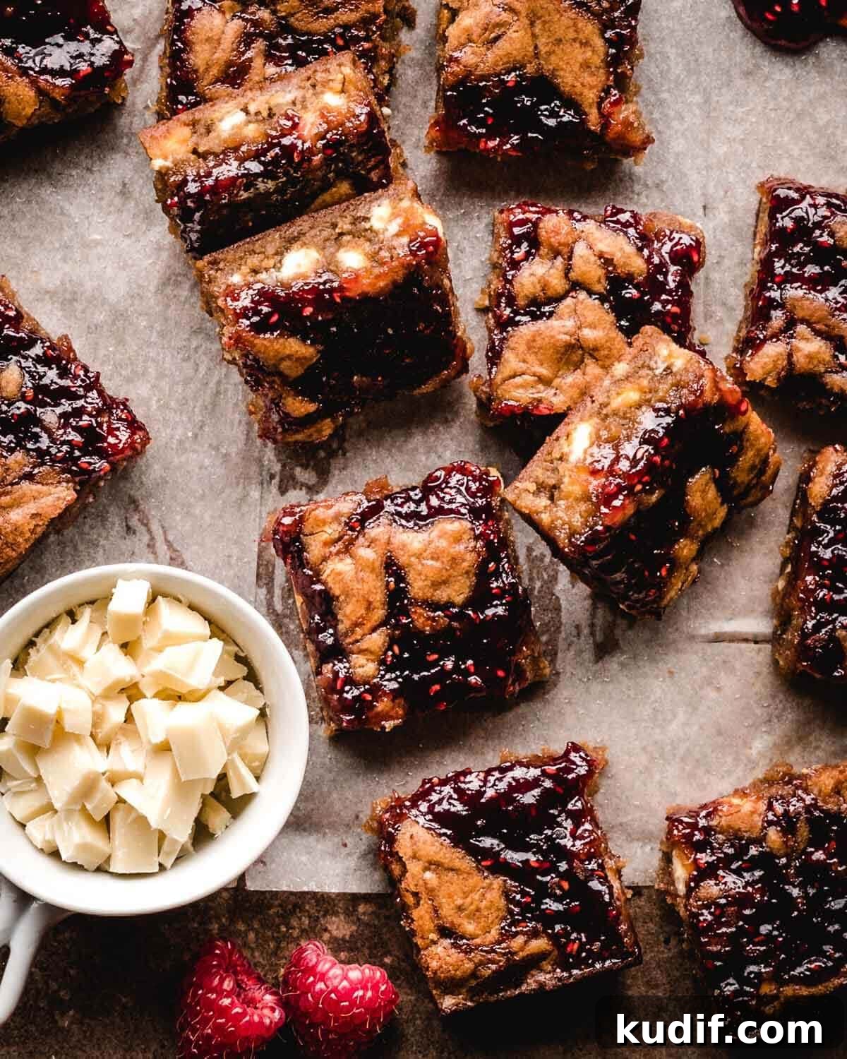 White Chocolate Raspberry Blondies with Tangy Fruit Swirls 14 Small pieces of white chocolate and raspberry blondies on parchment paper.