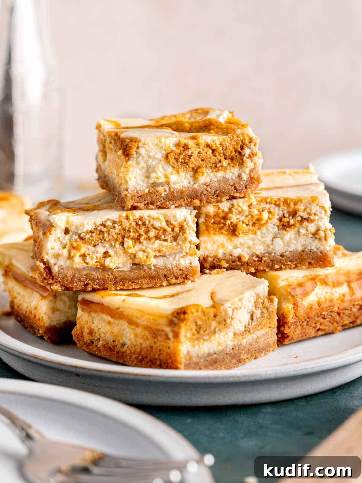 Pumpkin Cheesecake Bars Recipe for Fall Dessert Lovers 2 Swirled pumpkin cheesecake bars stacked on a plate.