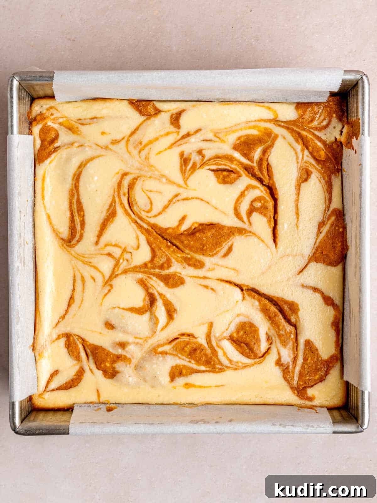 Pumpkin Cheesecake Bars Recipe for Fall Dessert Lovers 10 Baked pumpkin swirl cheesecake bars in a parchment lined pan.
