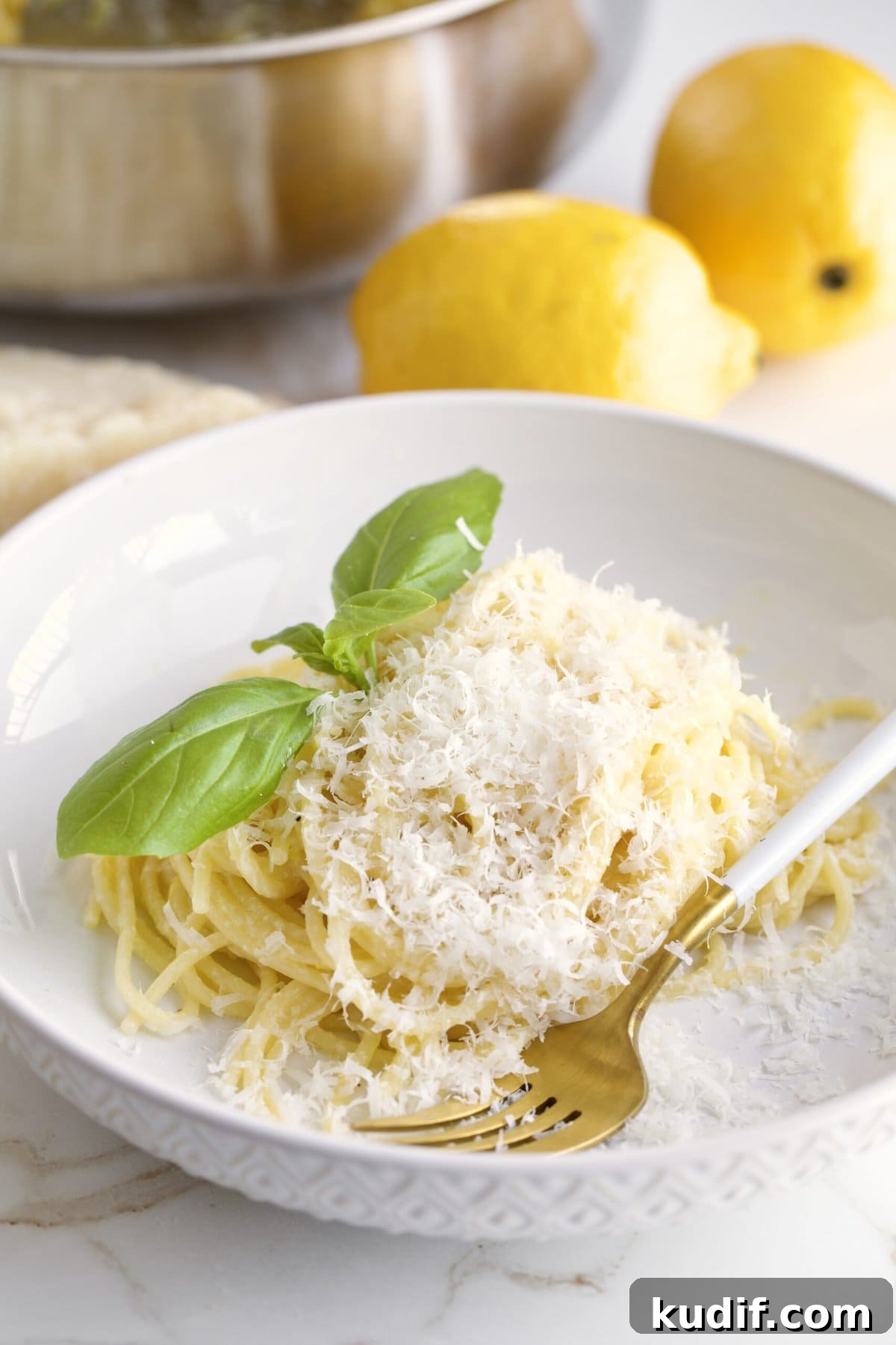 Creamy Lemon Butter Pasta Recipe (Pasta al Limone) 9 A bowl of pasta al limone on the table with lemons and a cooking pan in the background.
