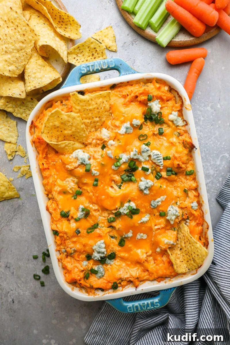 Lightened-Up Buffalo Chicken Dip Recipe for Game Day 7 A casserole dish filled with buffalo chicken dip surrounded by tortillas chips, fresh celery sticks and baby carrots
