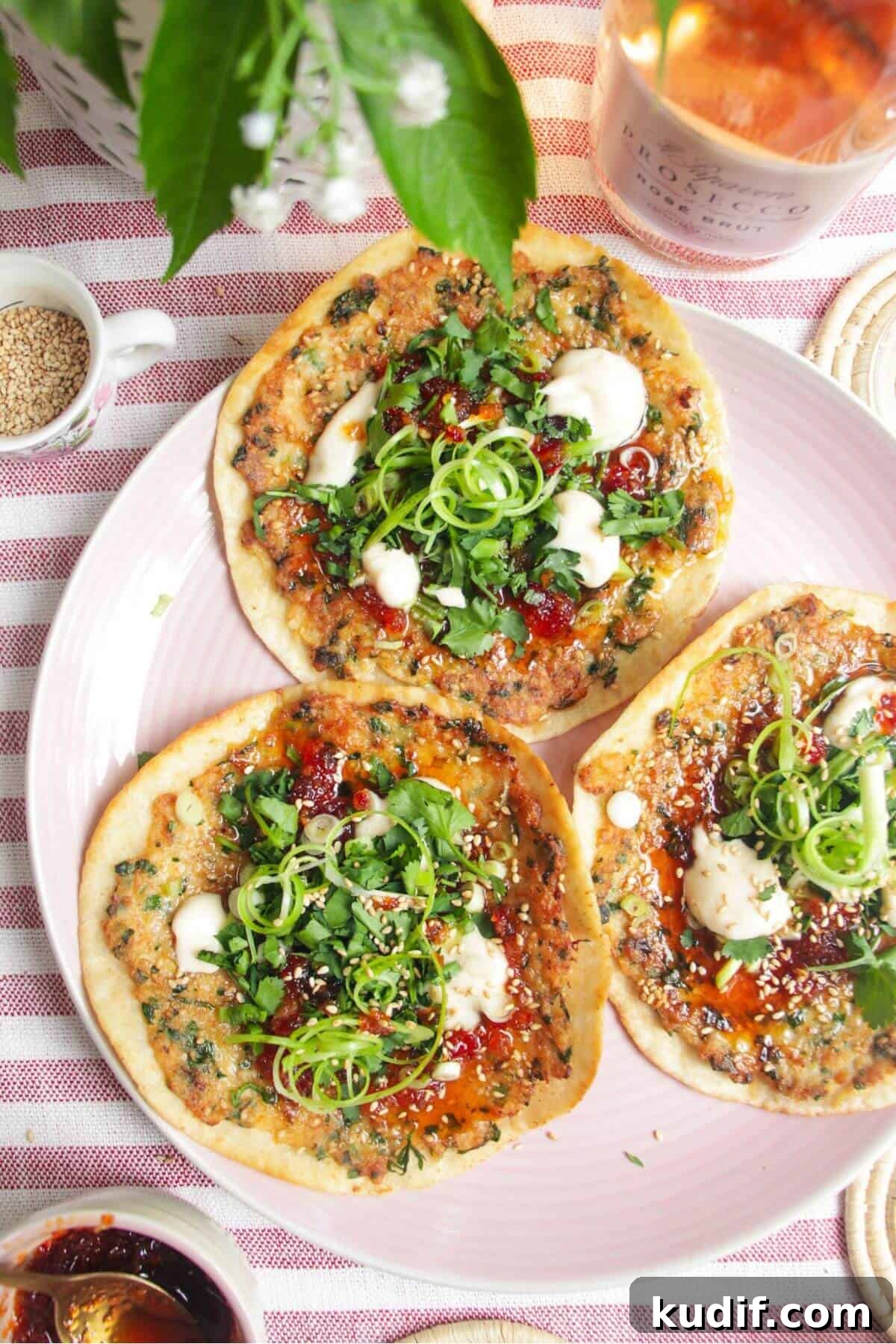 Smash Shrimp Toast Tacos — Crispy Prawn Toast Taco Recipe 14 Three prawn toast tacos topped with herbs and aioli on a pink plate.