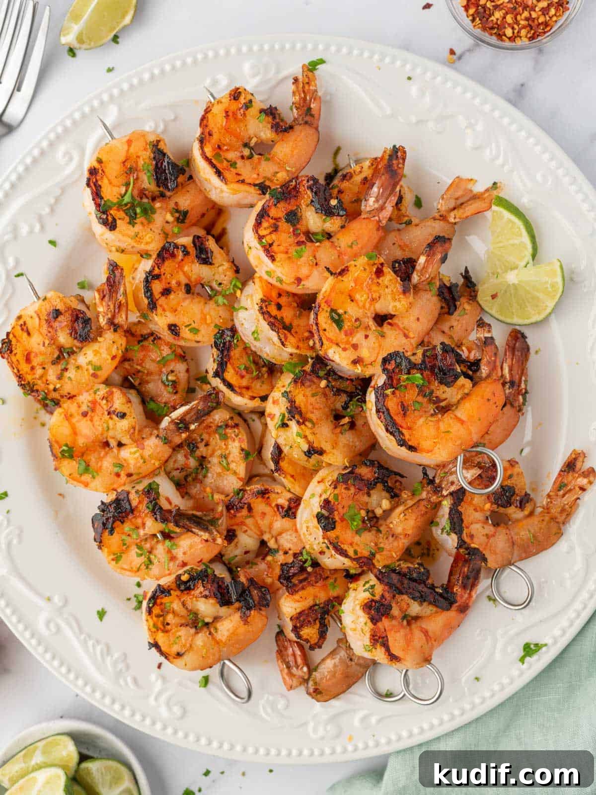 Garlic Grilled Shrimp Kabobs Recipe for Summer BBQ 2 Honey lime shrimp skewers stacked on a plate with lime wedges.