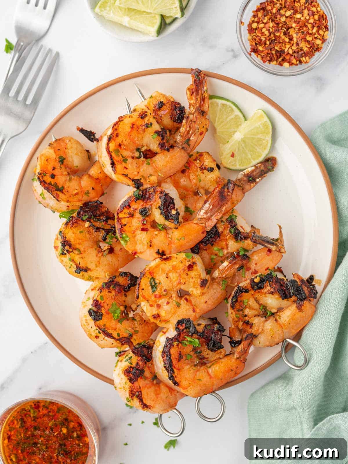 Garlic Grilled Shrimp Kabobs Recipe for Summer BBQ 6 Garlic shrimp skewers on a plate with forks on the side.
