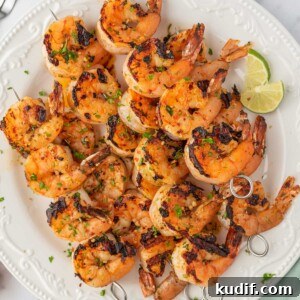 Garlic Grilled Shrimp Kabobs Recipe for Summer BBQ 8 Honey lime shrimp skewers stacked on a plate with lime wedges.
