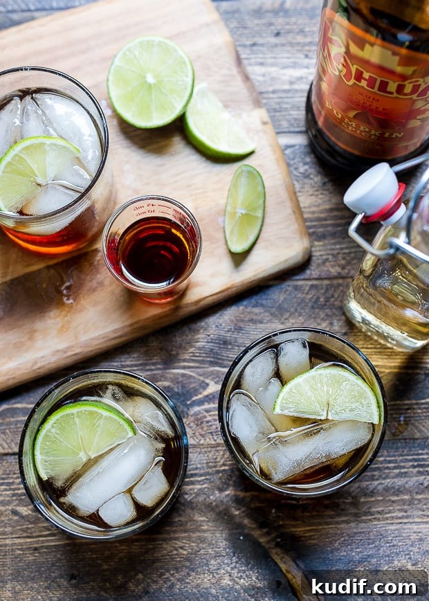 Pumpkin Spice Dark & Stormy Cocktail Recipe for Fall Nights 6 Cocktails on a wooden surface surrounded by a cutting board, slices of lime, ginger beer and Kahlúa Pumpkin Spice.