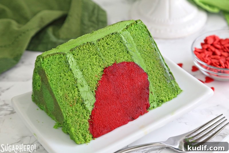 Grinch Cake - close-up of one slice of Grinch cake, made from green cake layers and a bright red heart inside | From SugarHero.com