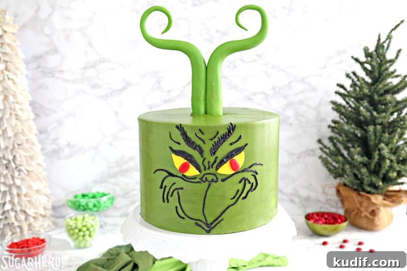 Grinch Cake - green cake with a Grinch face piped in black buttercream, and green Grinch fondant hair | From SugarHero.com