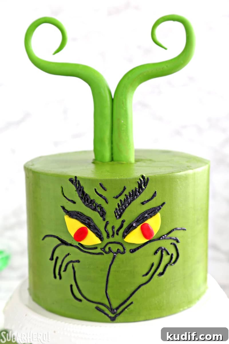 Grinch Cake - closer shot of the Grinch face piped onto a green cake with fondant hair | From SugarHero.com