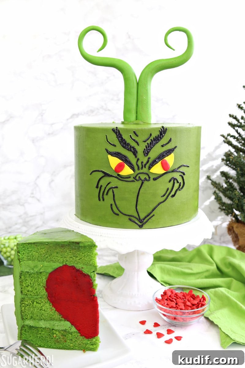 Grinch Cake - front of Grinch cake on a cake stand, with a slice of cake showing the red heart inside | From SugarHero.com