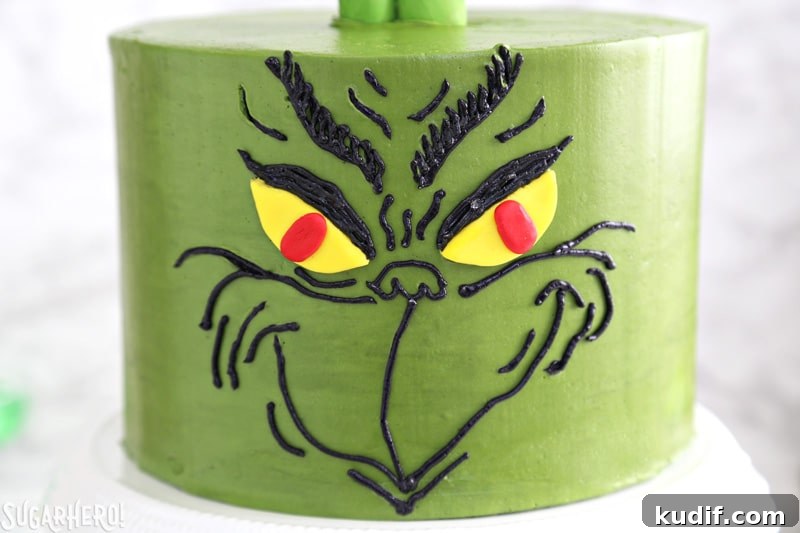 Grinch Cake - close-up of the Grinch's face, done in black buttercream on a green cake | From SugarHero.com