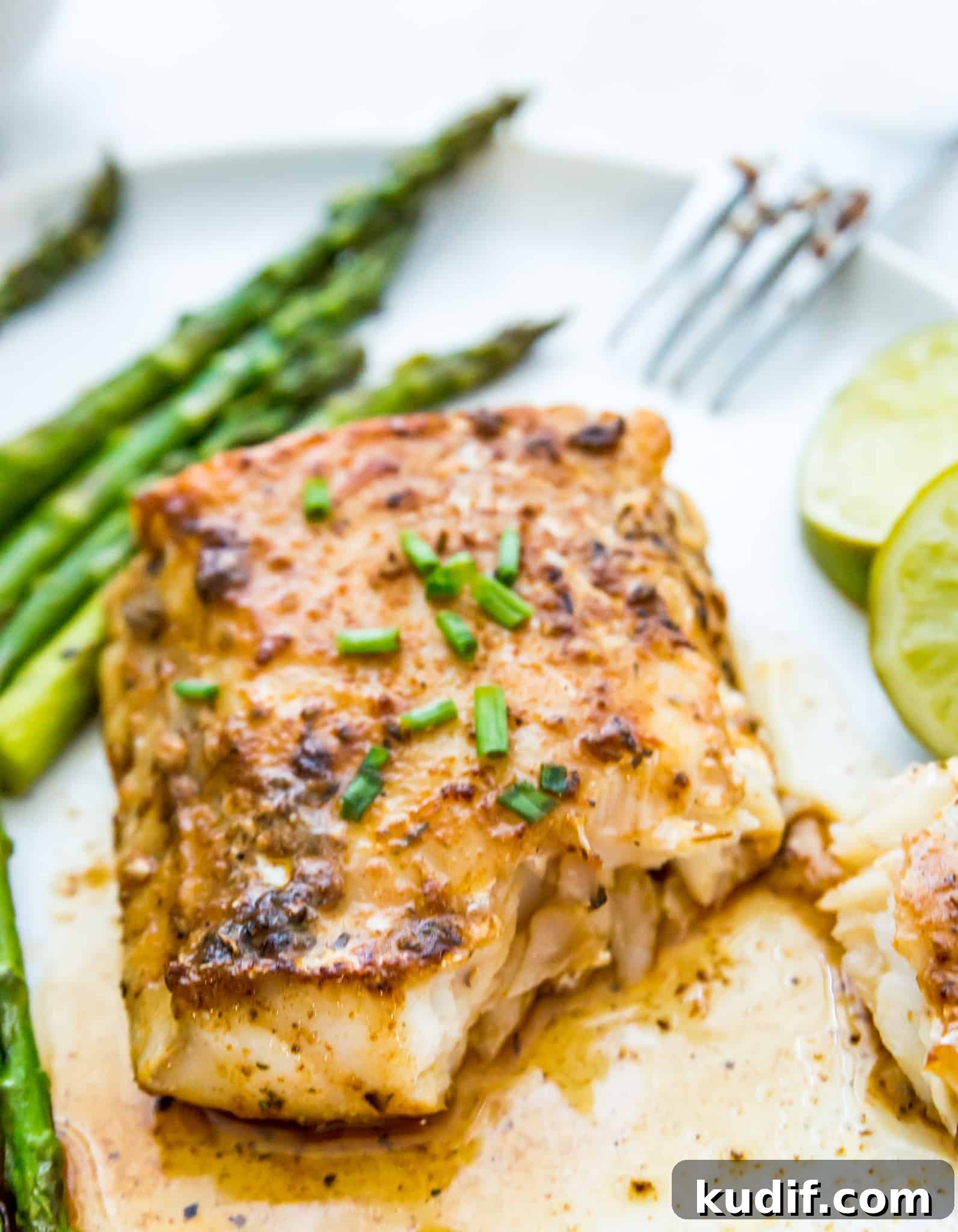 A piece of cooked cod on a plate with asparagus and a lime wedge next to it.