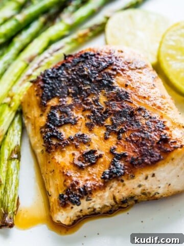A piece of blackened mahi mahi on a plate with cooked asparagus and lime wedges beside it.