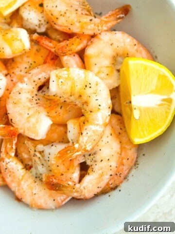 A bowl of cooked shrimp with lemon wedges beside them.