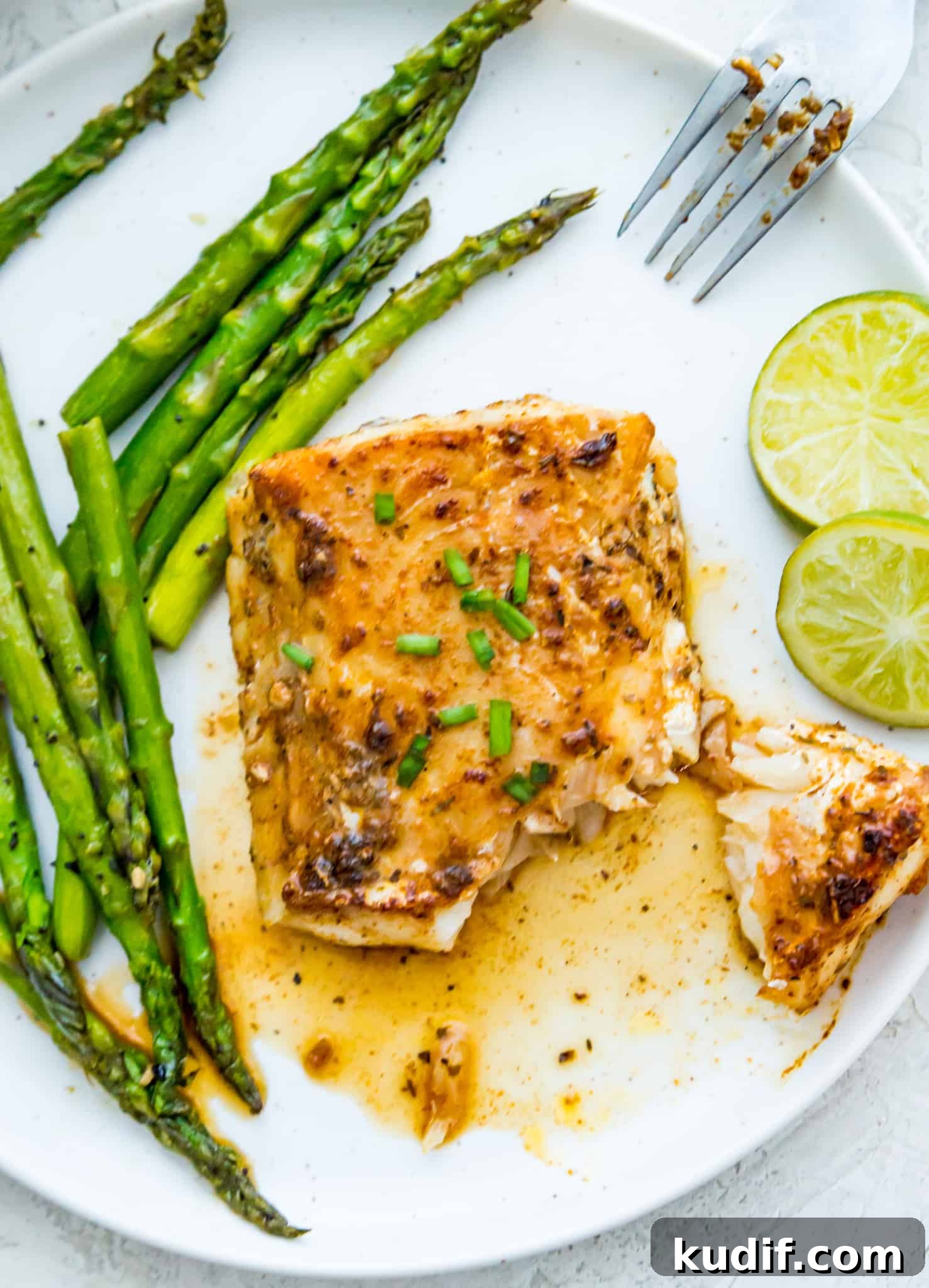 A plate with a piece of blackened cod on it with cooked asparagus and a lime wedge next to it.
