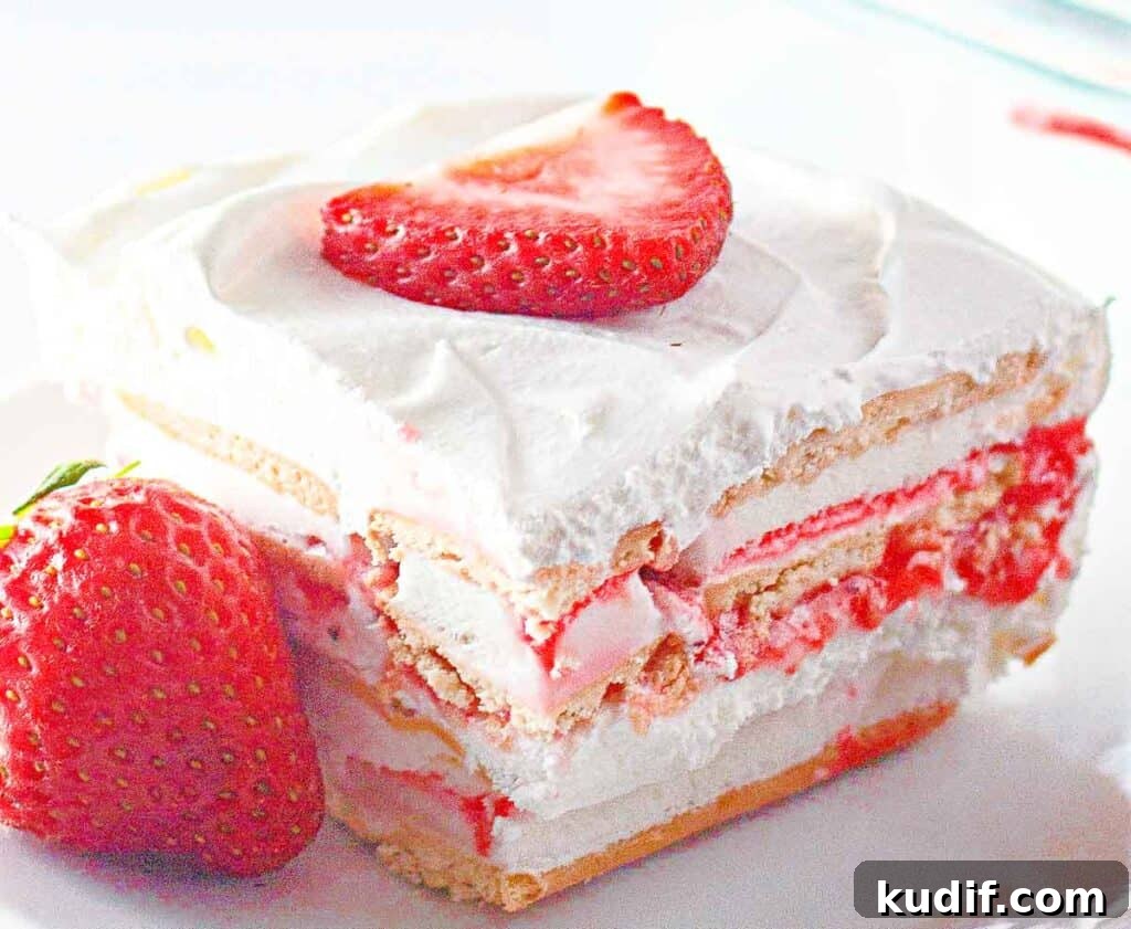 Quick Berry Desserts to Satisfy Sweet Cravings Fast 15 A slice of strawberry icebox cake with layers of whipped cream, graham crackers, and strawberry slices, topped with a strawberry piece.
