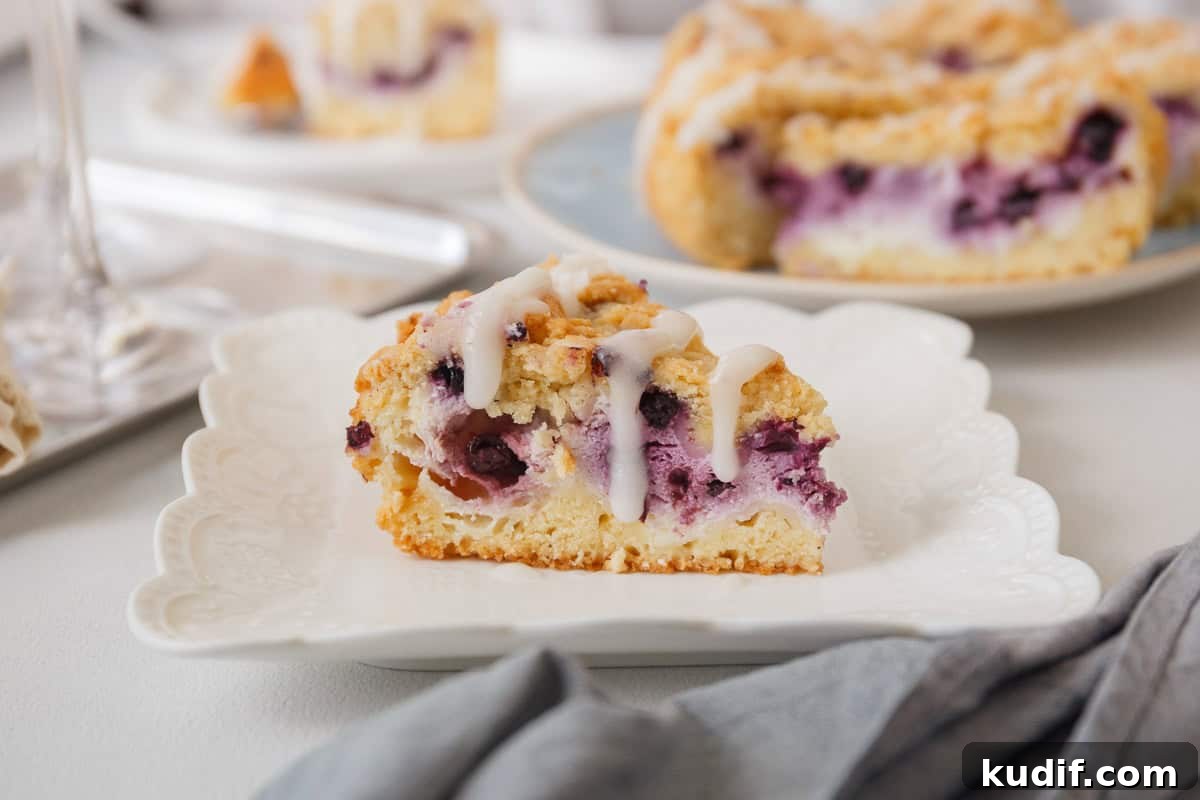 Quick Berry Desserts to Satisfy Sweet Cravings Fast 9 A slice of blueberry cheesecake crumbcake on a white plate.