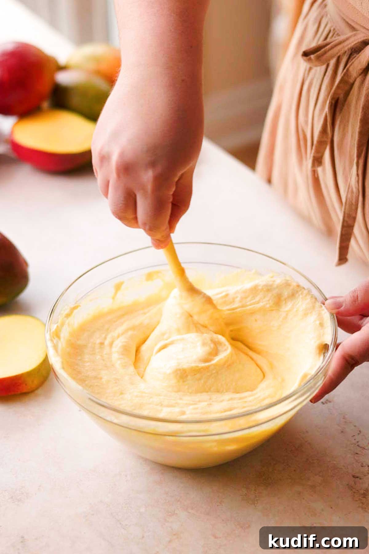 Mango Crepe Cake Recipe with Homemade Crepes Made from Scratch 13 folding the mango pure into whipped cream with a spatula in a glass bowl