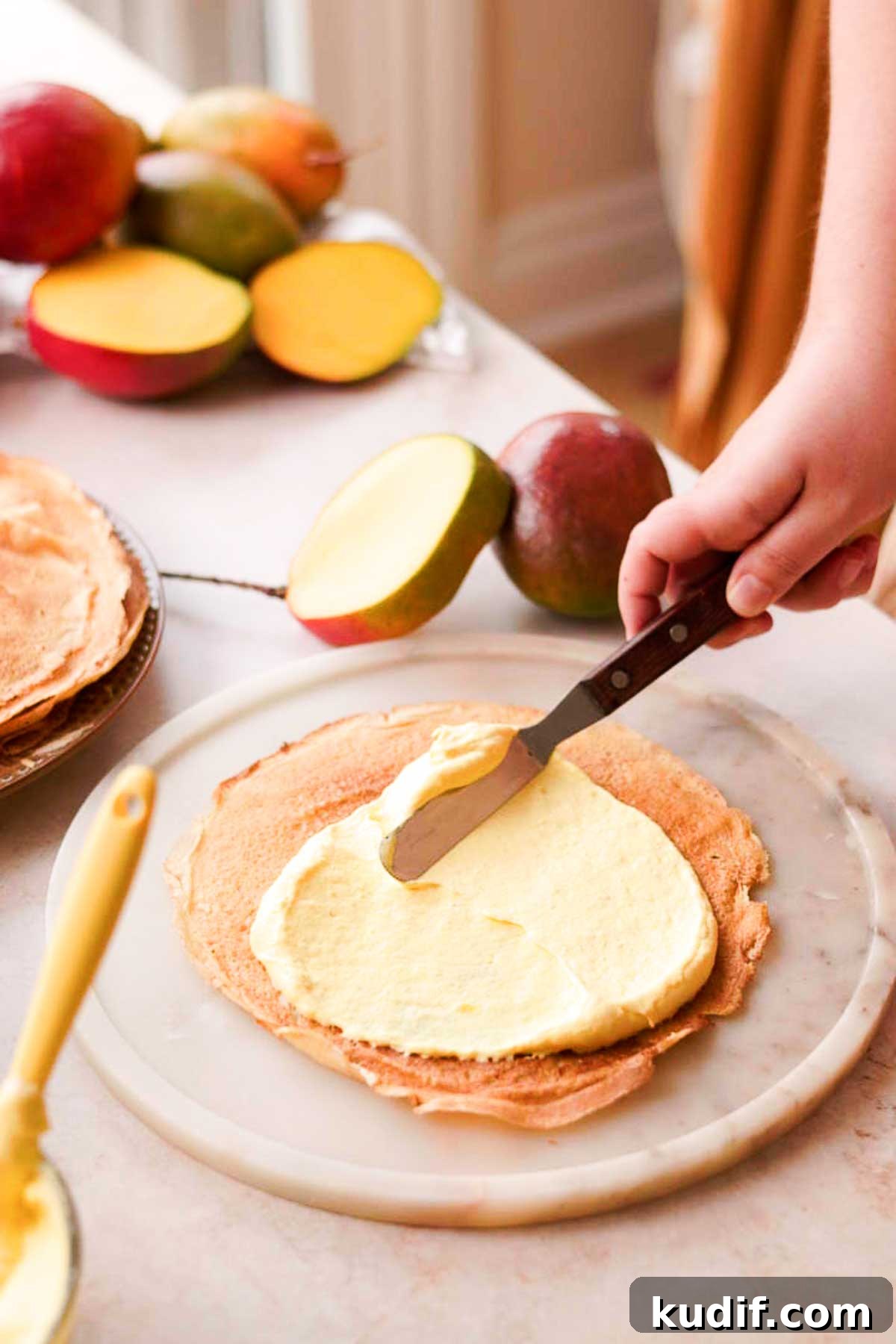 Mango Crepe Cake Recipe with Homemade Crepes Made from Scratch 14 spreading mango filling onto a crepe with a metal spatula